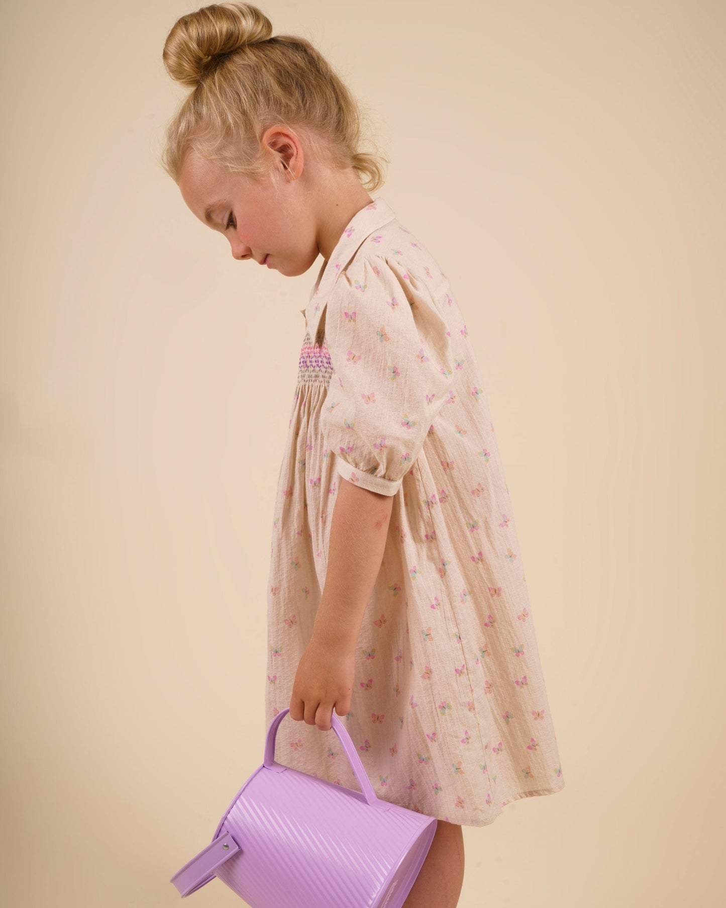 Early Sunday, Jane Dress in Butterfly Print color, made from printed cotton tiny swiss dobby fabric, featuring Smocked / embroidered yoke, peter pan collar and puffed short sleeves, shown in a side view of model wearing it