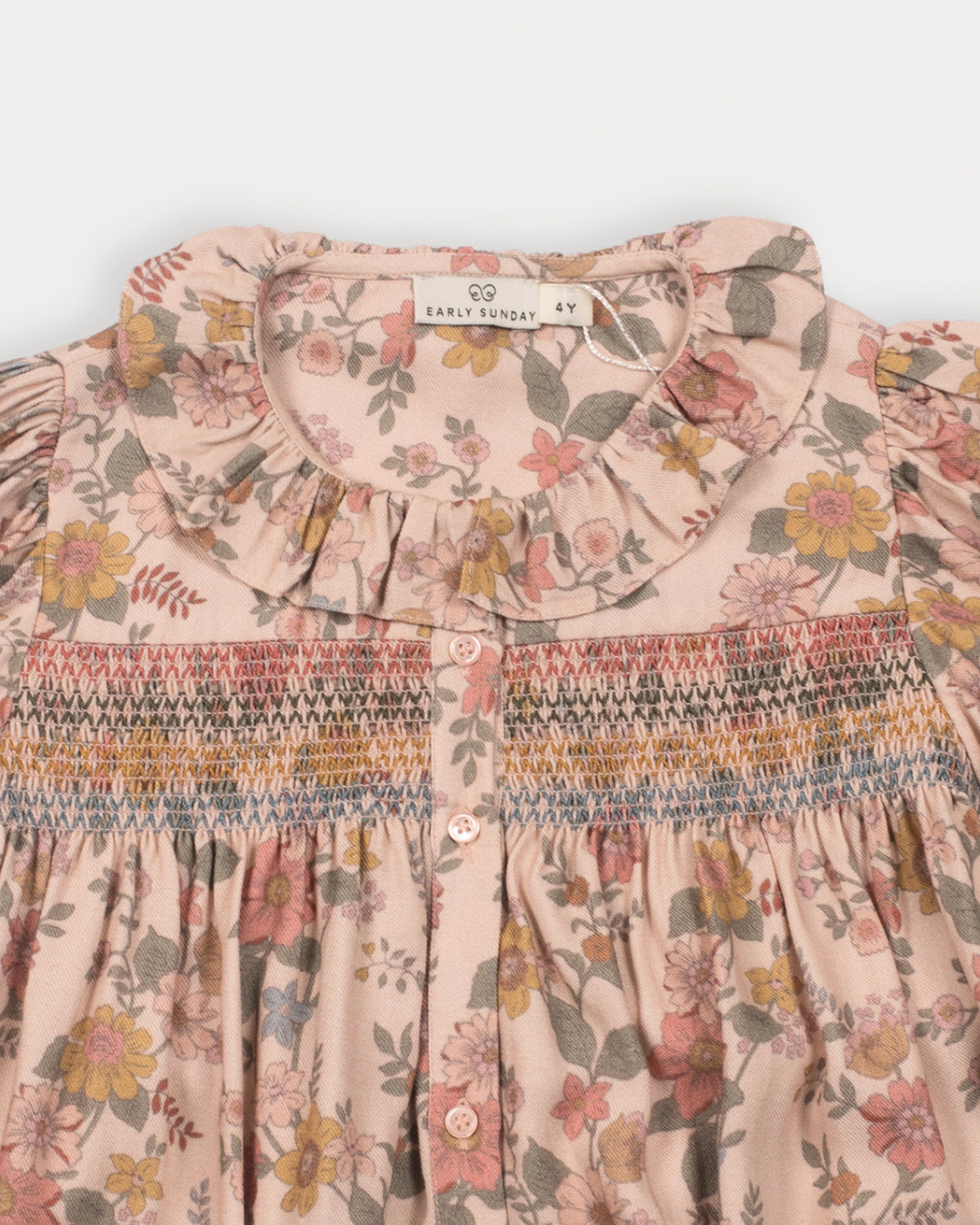 Early Sunday, Jeanette Dress in Bloom, made from Printed Viscose Twill fabric, featuring smocked chest with frilled neckline and soft gathered puff sleeves, shown in a closeup flat-lay view