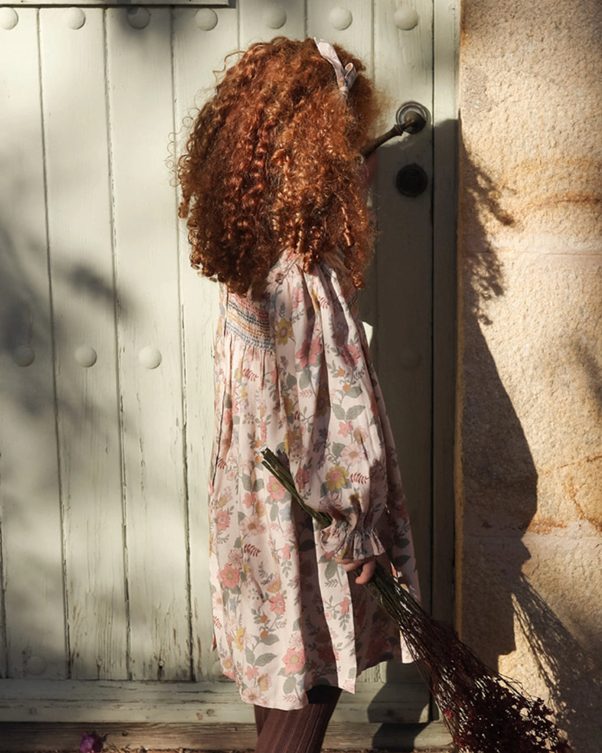 Early Sunday, Jeanette Dress in Bloom, made from Printed Viscose Twill fabric, featuring smocked chest with frilled neckline and soft gathered puff sleeves, shown in a side view of model wearing outdoors
