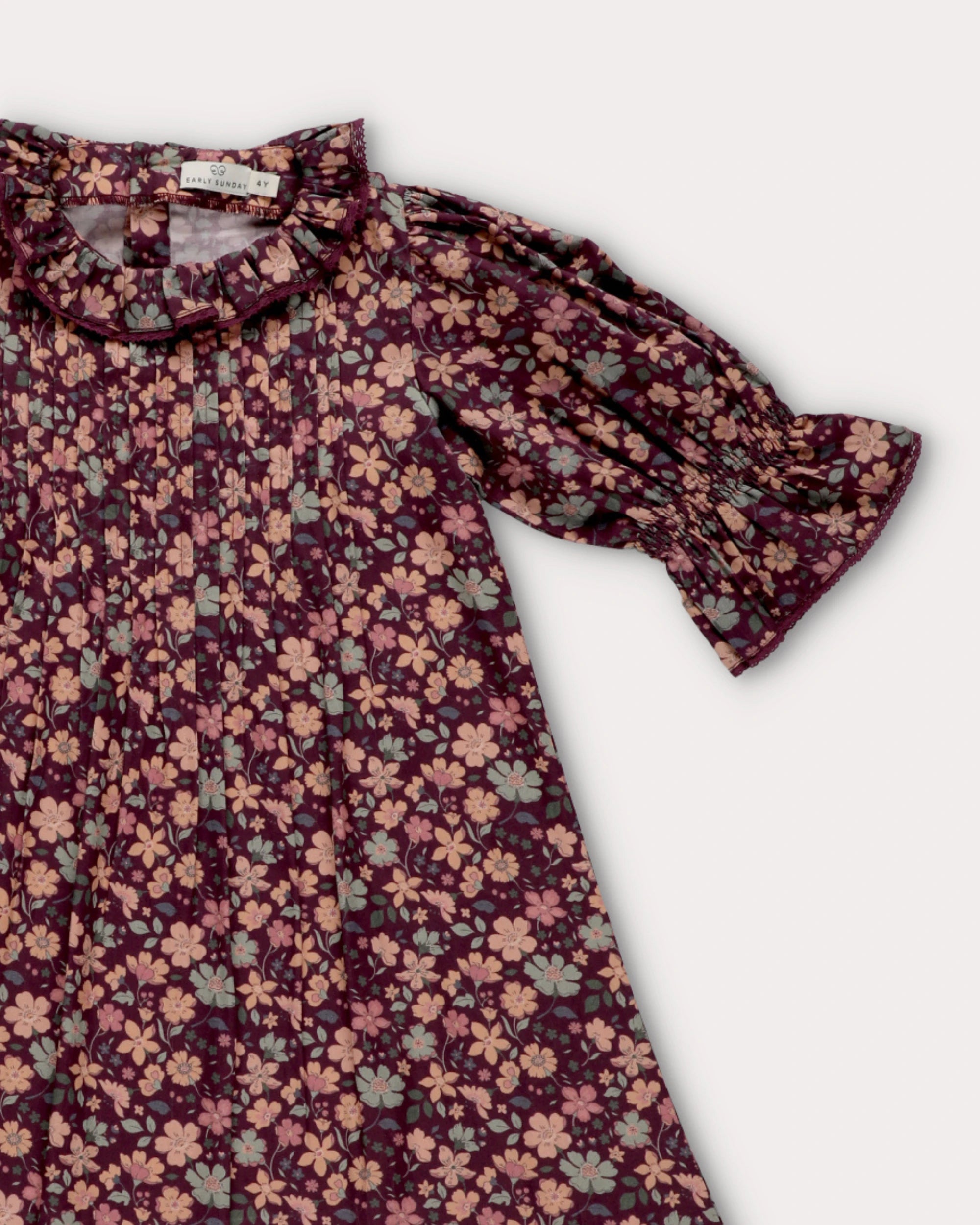 Early Sunday, Julie Dress in Plum, made from Printed Cotton Satin fabric, featuring detailed lace gathered sleeves with frilled neckline & floral detailing, shown in a closeup flat-lay view