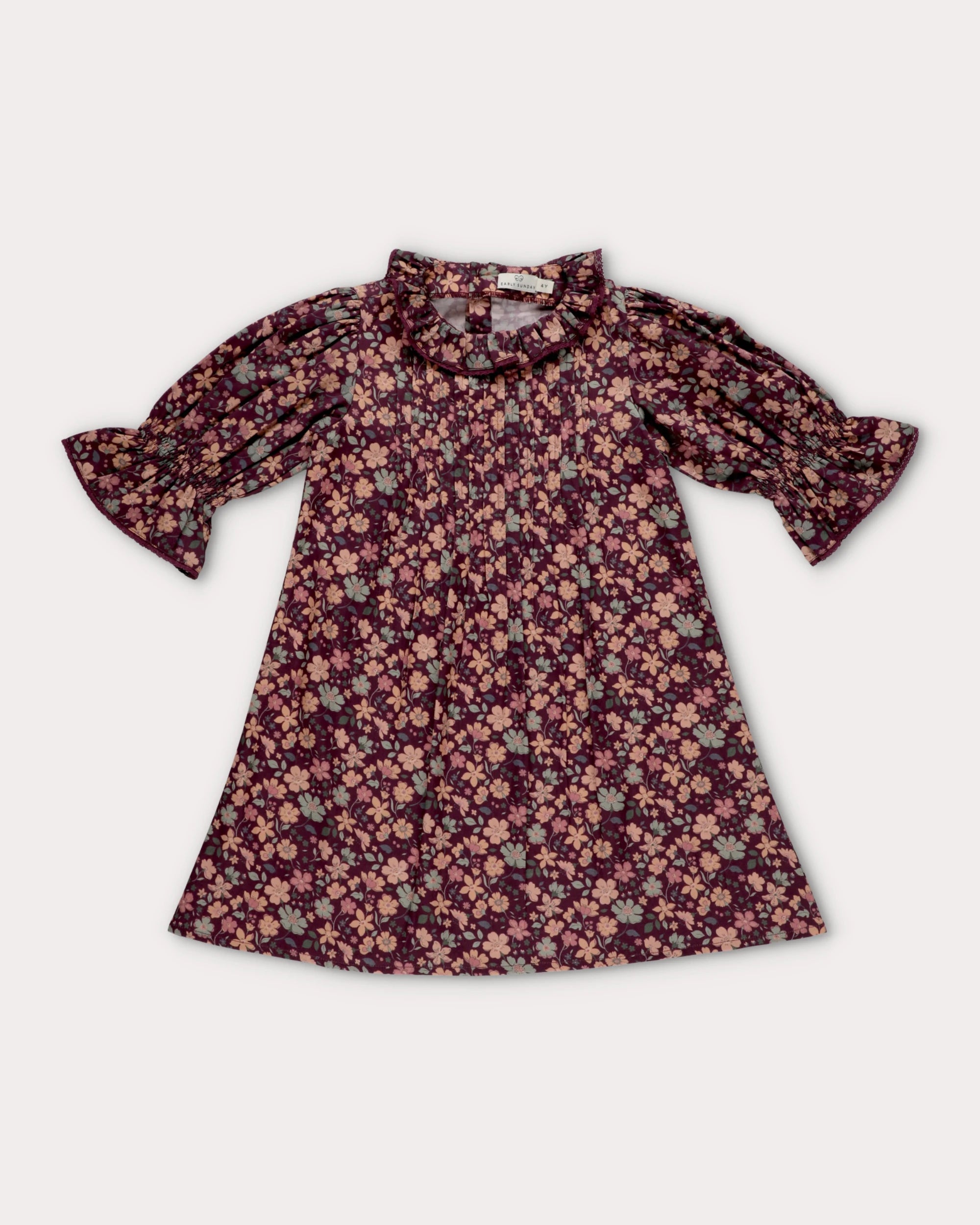 Early Sunday, Julie Dress in Plum, made from Printed Cotton Satin fabric, featuring detailed lace gathered sleeves with frilled neckline & floral detailing, shown in a front flat-lay view
