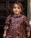 Early Sunday, Julie Dress in Plum, made from Printed Cotton Satin fabric, featuring detailed lace gathered sleeves with frilled neckline & floral detailing, shown in a front view of model wearing it