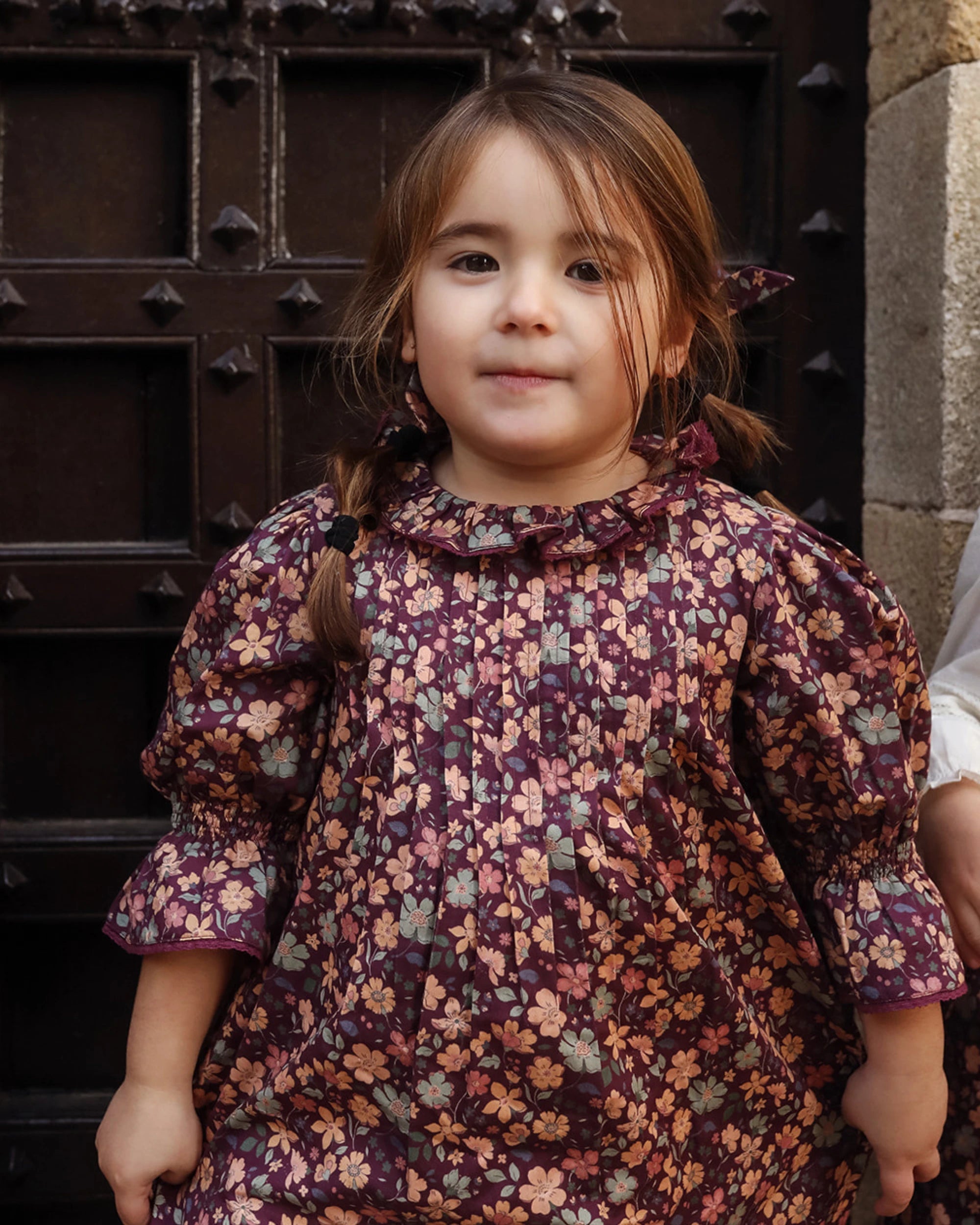 Early Sunday, Julie Dress in Plum, made from Printed Cotton Satin fabric, featuring detailed lace gathered sleeves with frilled neckline & floral detailing, shown in a front view of model wearing it
