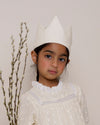 Early Sunday, Kids Crown in Hazelnut cream color, made from All over Embroidered Cotton Cambric fabric, featuring a design with pointed tips & an elasticated band, shown in an angled view of model wearing it