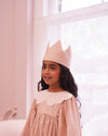 Early Sunday, Kids Crown in Feather print, made from Printed 60s Cotton Cambric fabric, featuring a design with pointed tips & an elasticated band, shown in an angled view of model wearing it in a close-up shot
