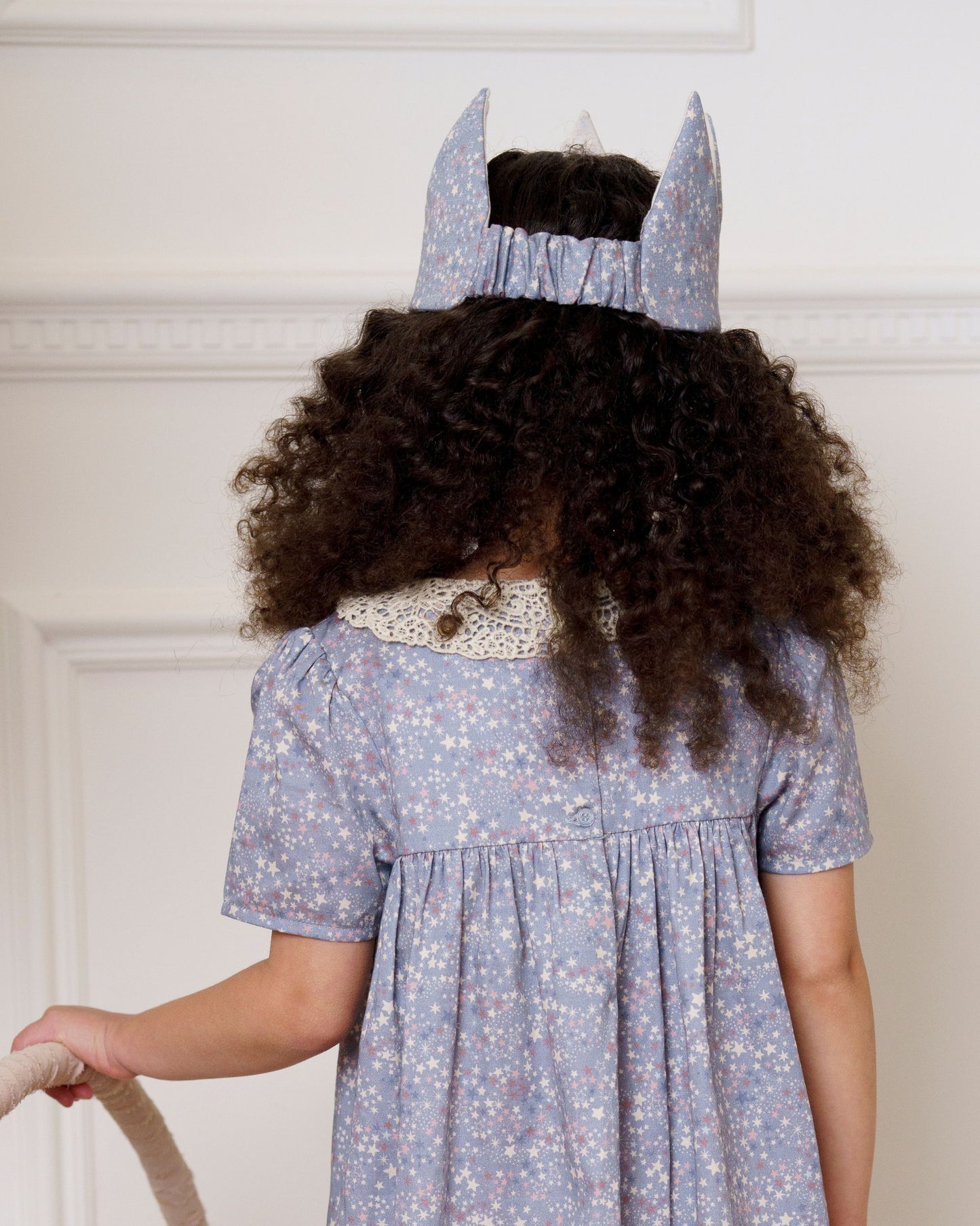 Early Sunday, Kids Crown in Celestial print, made from Printed 60s Cotton Satin fabric, featuring a design with pointed tips & an elasticated band, shown in a back view of model wearing it