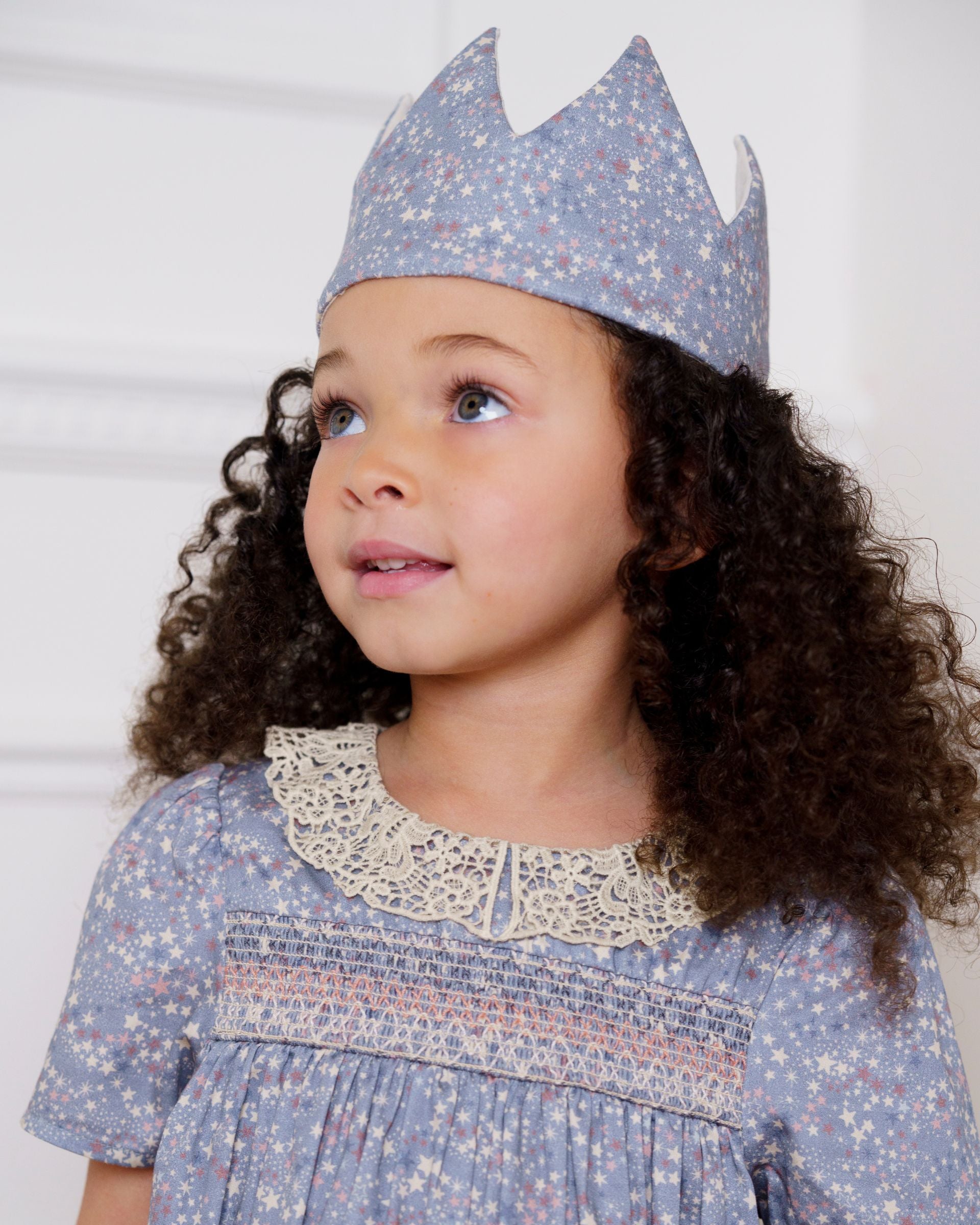 Early Sunday, Kids Crown in Celestial print, made from Printed 60s Cotton Satin fabric, featuring a design with pointed tips & an elasticated band, shown in a close up shot of model wearing it