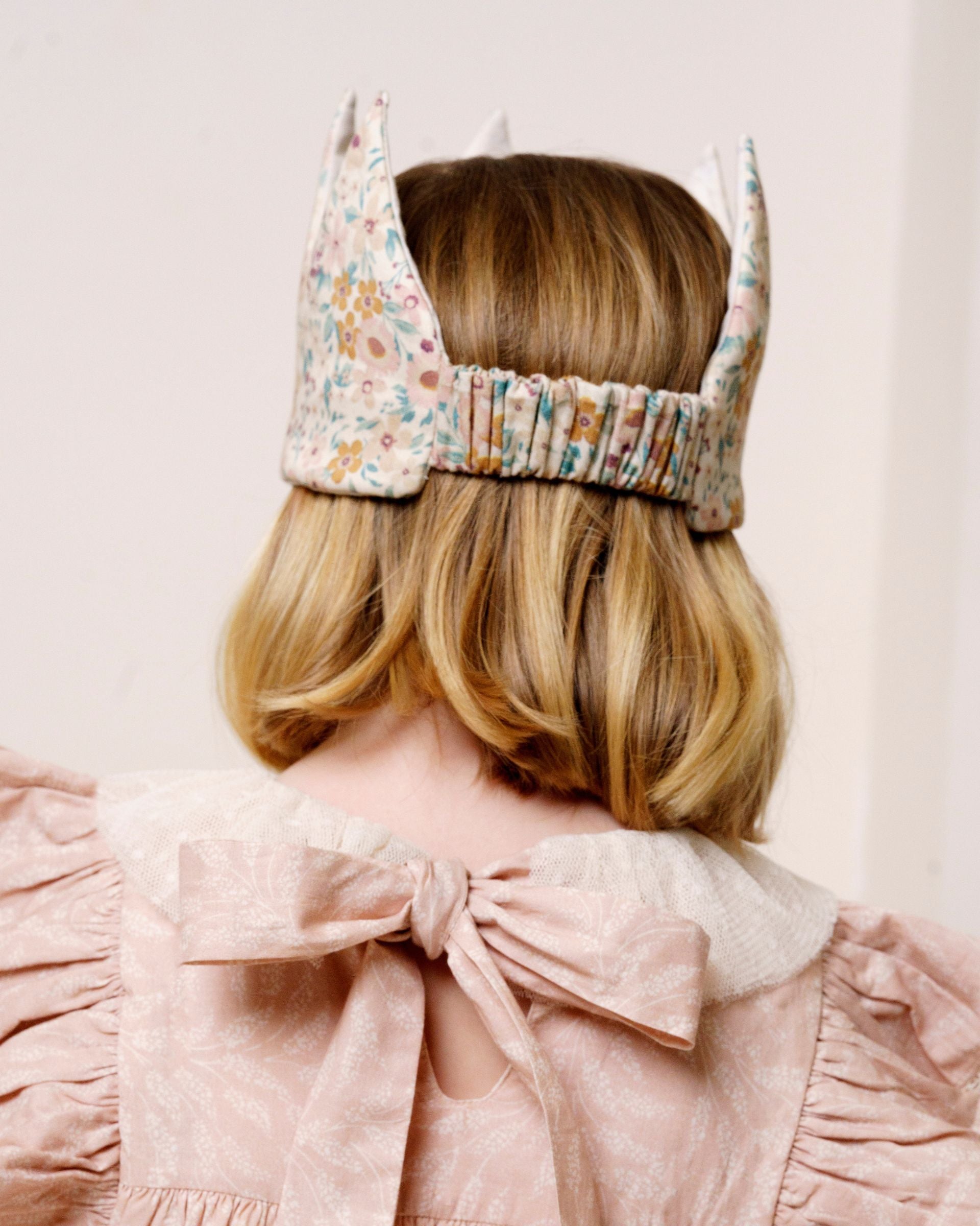 Early Sunday, Kids Crown in Floral print, made from Printed 60s Cotton Satin fabric, featuring a design with pointed tips & an elasticated band, shown in a back view of model wearing it