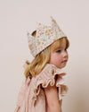 Early Sunday, Kids Crown in Floral print, made from Printed 60s Cotton Satin fabric, featuring a design with pointed tips & an elasticated band, shown in a close-up side view of a model wearing it