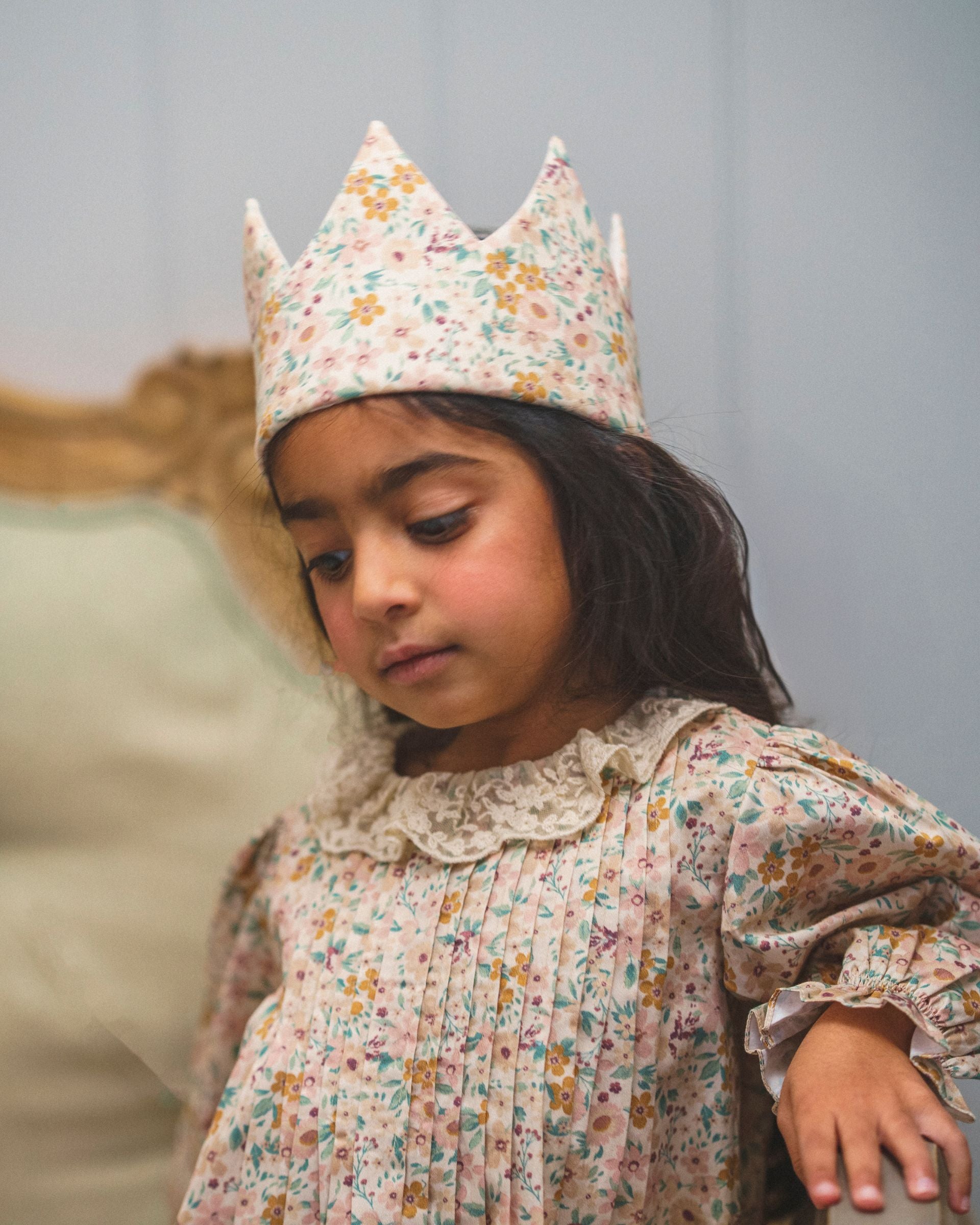 Early Sunday, Kids Crown in Floral print, made from Printed 60s Cotton Satin fabric, featuring a design with pointed tips & an elasticated band, shown in a an angled view of a model wearing it