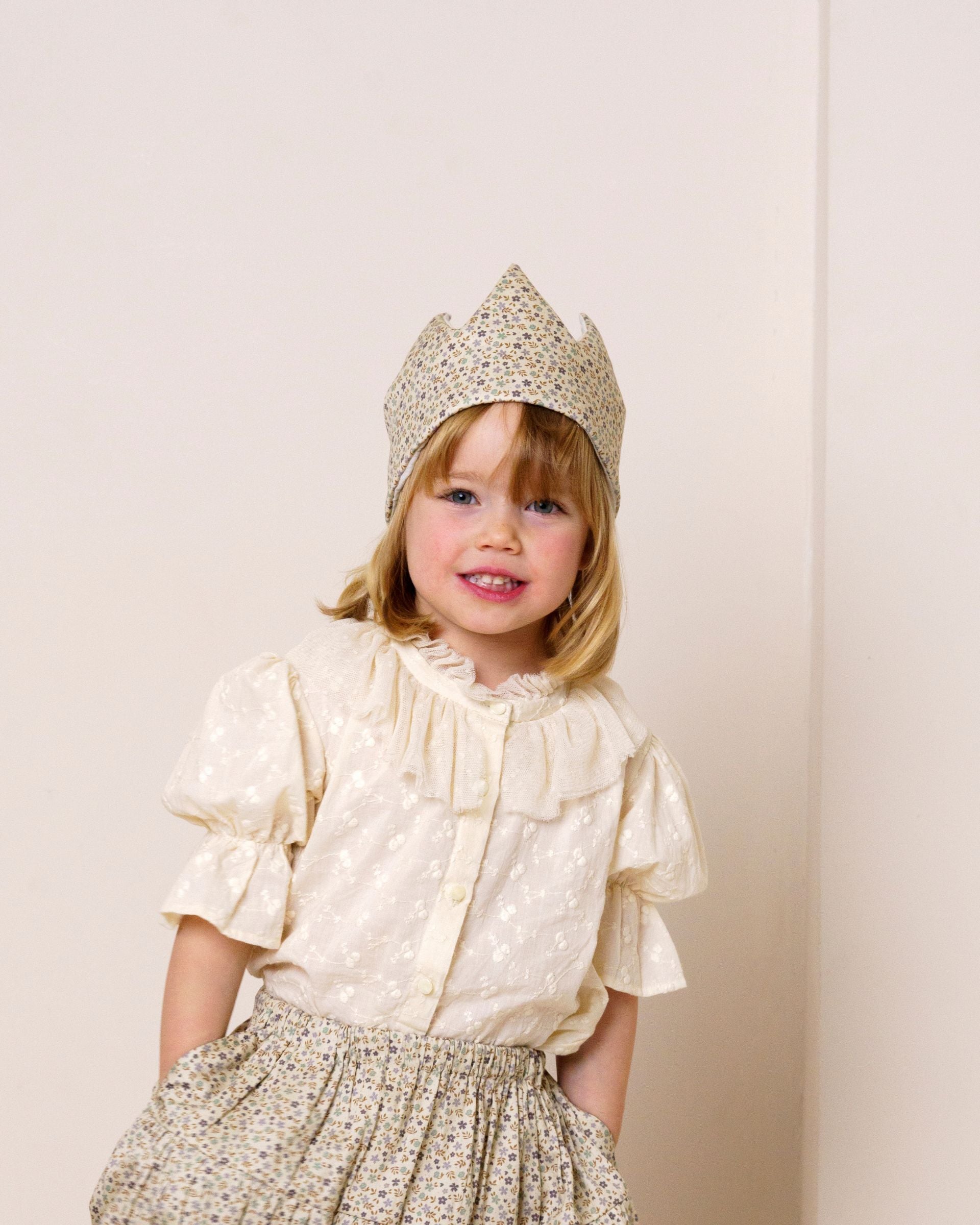 Early Sunday, Kids Crown in Mini Flowers print, made from Printed 60s Cotton Satin fabric, featuring a design with pointed tips & an elasticated band, shown in a front view of model wearing it