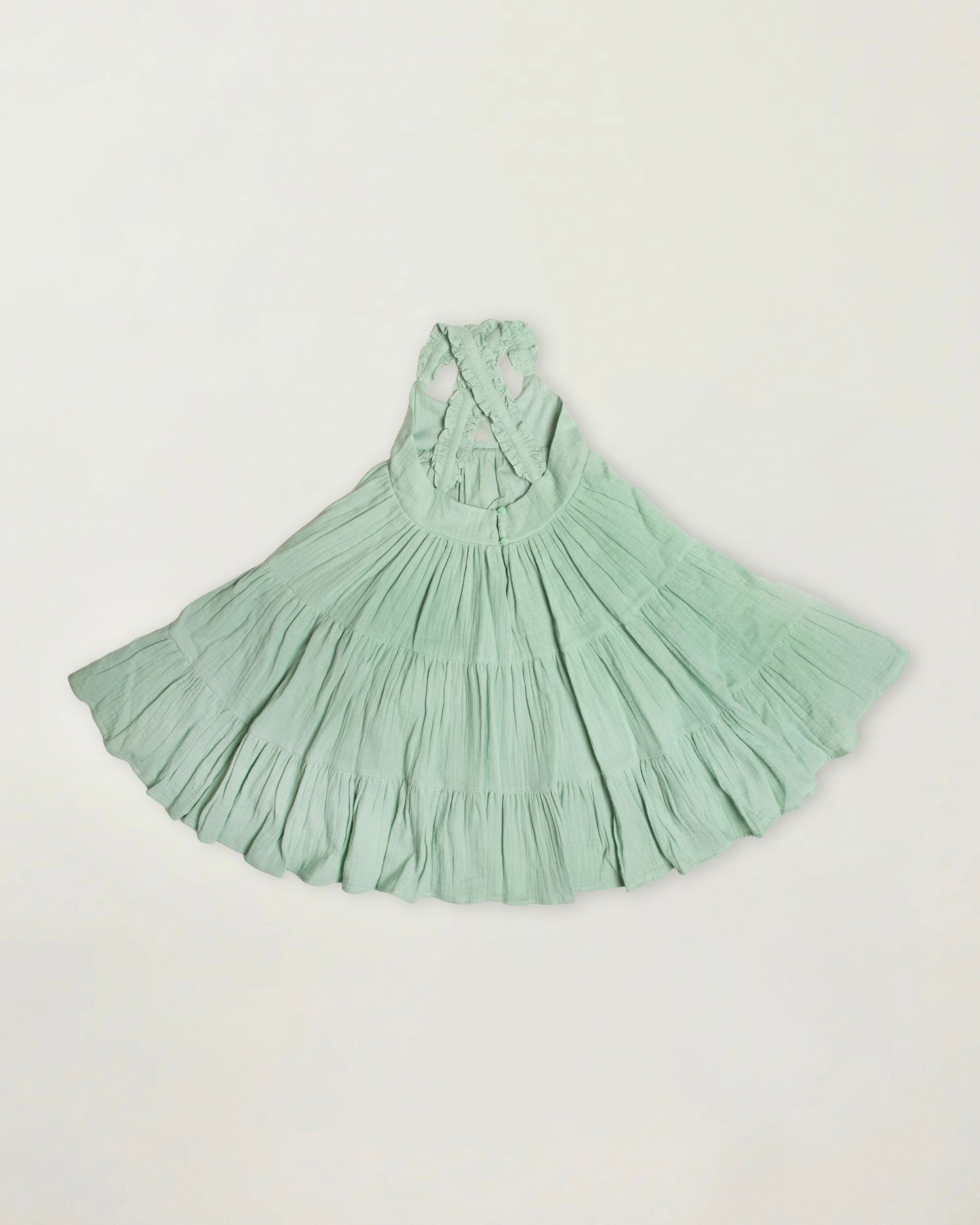Early Sunday, Laura Dress in Mint color, made from 100% cotton double gauze solid fabric, featuring Crisscross ruffle straps with delicate trim accents and a softly gathered tiered skirt, shown in a back flat-lay view