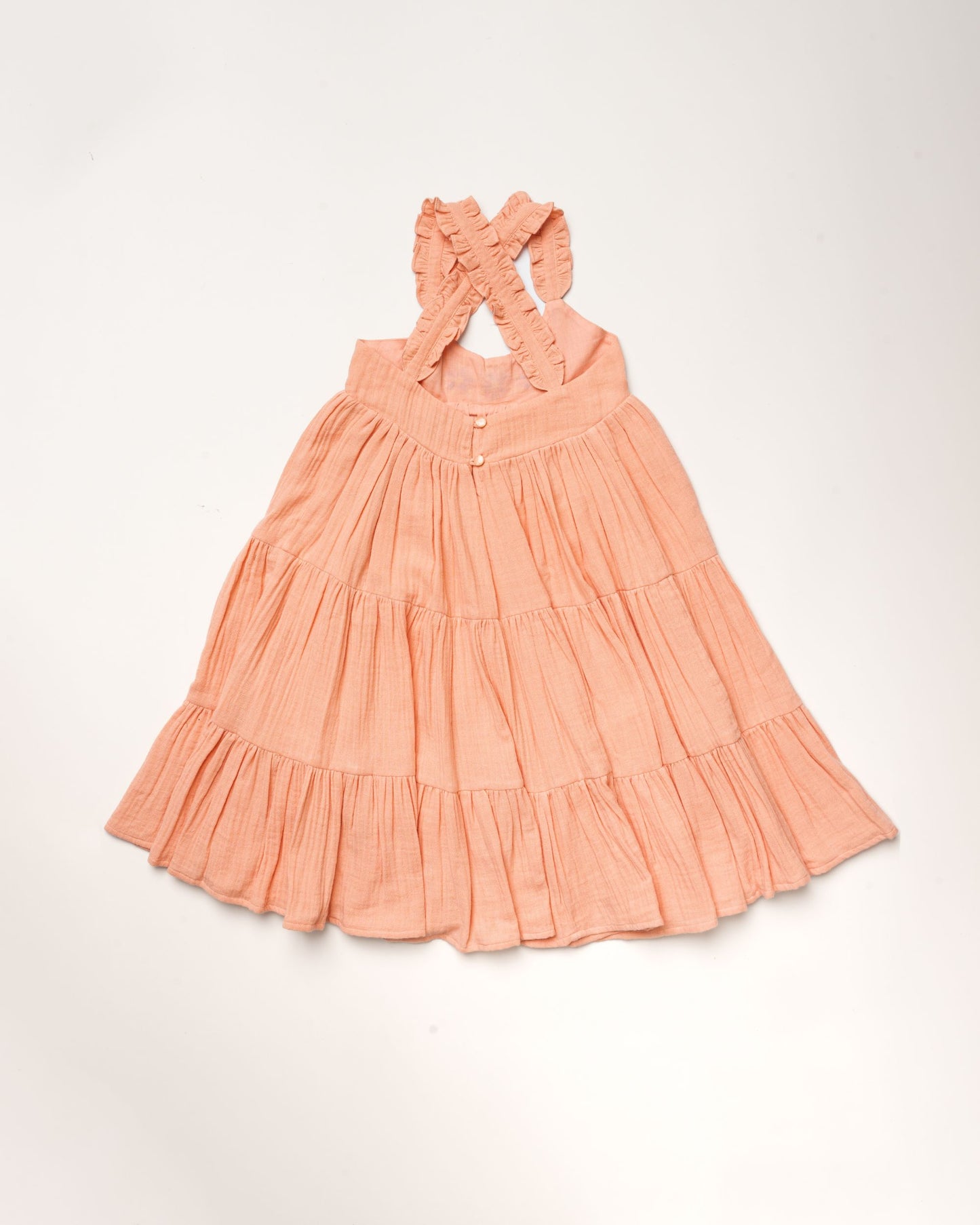 Early Sunday, Laura Dress in Candy Floss color, made from 100% cotton double gauze solid fabric, featuring Crisscross ruffle straps with delicate trim accents and a softly gathered tiered skirt, shown in a back flat-lay view