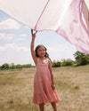 Early Sunday, Laura Dress in Candy Floss color, made from 100% cotton double gauze solid fabric, featuring Crisscross ruffle straps with delicate trim accents and a softly gathered tiered skirt, shown in a model wearing outdoors