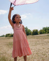 Early Sunday, Laura Dress in Candy Floss color, made from 100% cotton double gauze solid fabric, featuring Crisscross ruffle straps with delicate trim accents and a softly gathered tiered skirt, shown in a model standing facing front wearing
