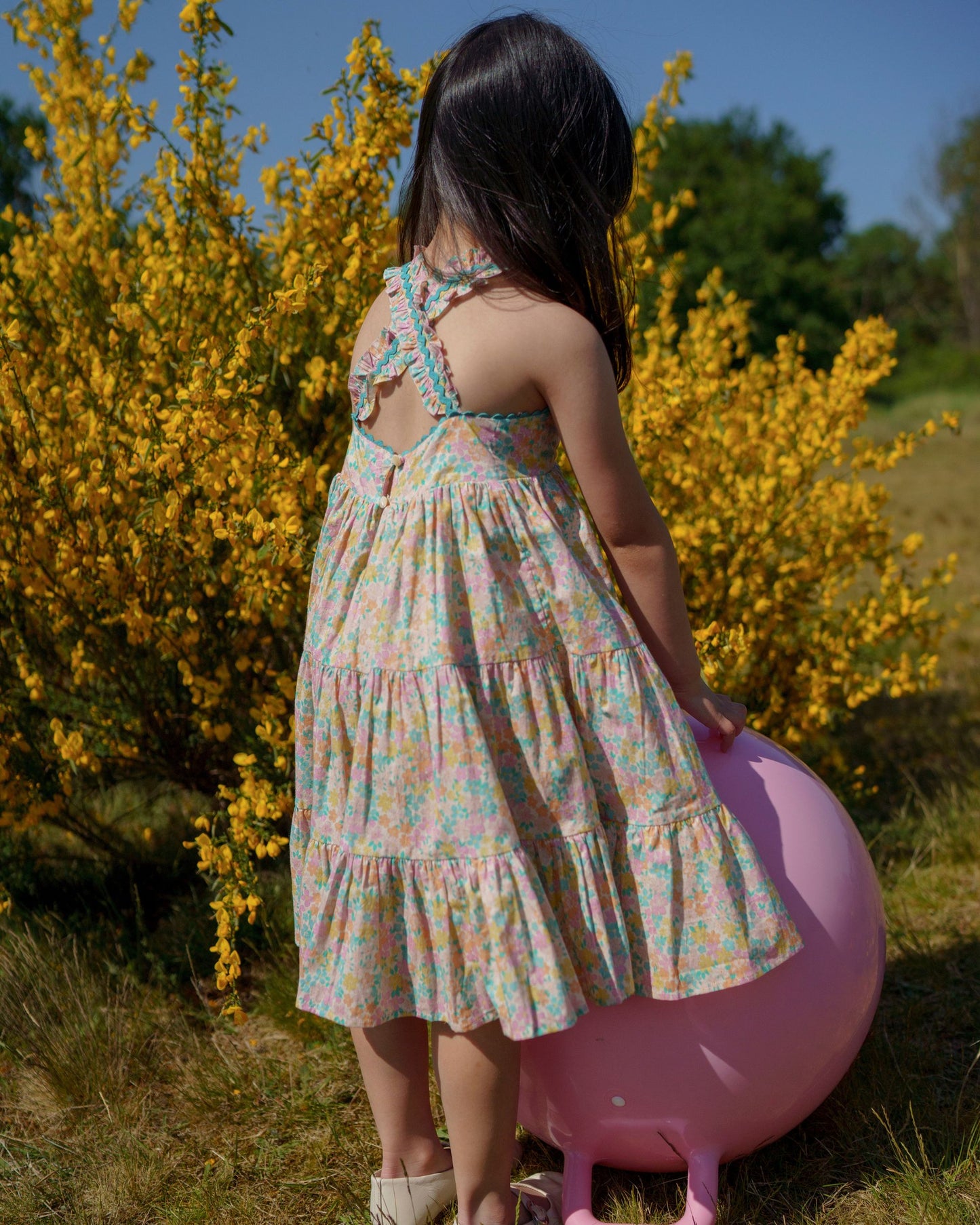 Early Sunday, Laura Dress in Emma Floral Mint color, made from printed 60s cotton cambric fabric, featuring Crisscross ruffle straps with delicate trim accents and a softly gathered tiered skirt, shown in a model wearing outdoors