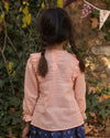 Early Sunday, Lauren Blouse in Blush, made from Cotton Jeera Dobby Voile fabric, featuring layered lace-trimmed ruffles and delicate pintuck detailing on the yoke, shown in a back view of model wearing outdoors