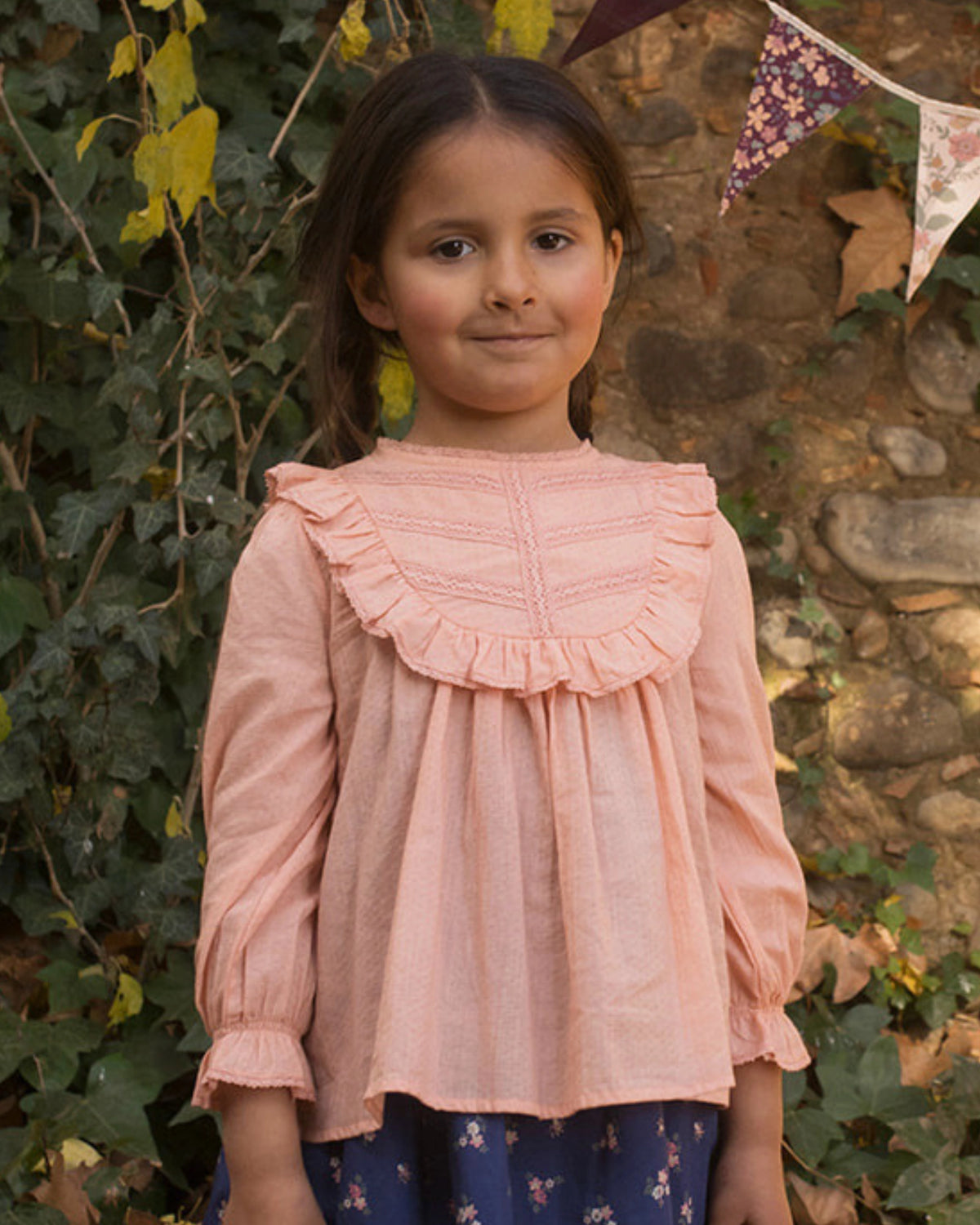 Early Sunday, Lauren Blouse in Blush, made from Cotton Jeera Dobby Voile fabric, featuring layered lace-trimmed ruffles and delicate pintuck detailing on the yoke, shown in a front view of model wearing outdoors