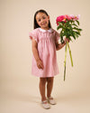 Early Sunday, Lila Dress in Peony color, made from 100% cotton gingham checks fabric, featuring Scalloped neckline with contrast stitching, flutter sleeves, gentle gathers, and embroidered hem detail, shown in a model standing facing front wearing