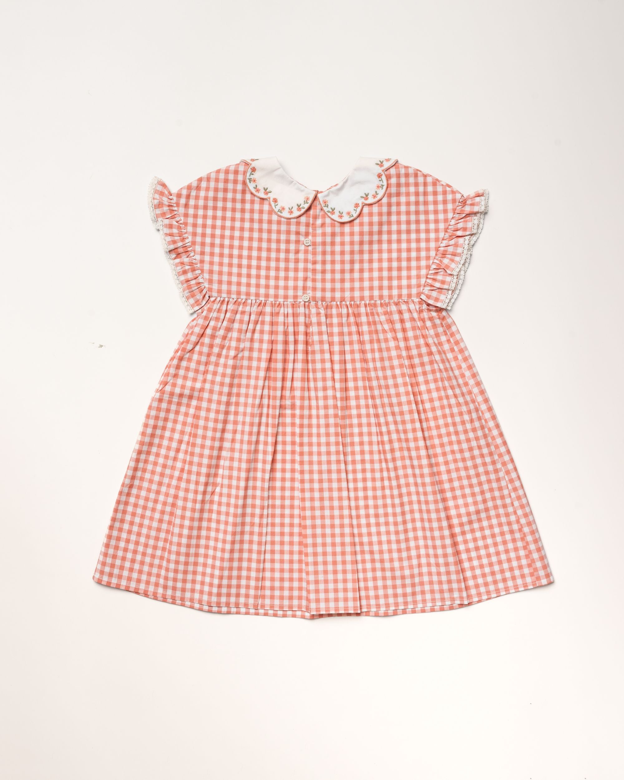 Early Sunday, Lila Dress in Peony color, made from 100% cotton gingham checks fabric, featuring Scalloped neckline with contrast stitching, flutter sleeves, gentle gathers, and embroidered hem detail, shown in a back flat-lay view
