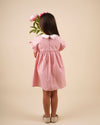 Early Sunday, Lila Dress in Peony color, made from 100% cotton gingham checks fabric, featuring Scalloped neckline with contrast stitching, flutter sleeves, gentle gathers, and embroidered hem detail, shown in a back view of model wearing