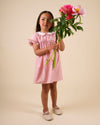 Early Sunday, Lila Dress in Peony color, made from 100% cotton gingham checks fabric, featuring Scalloped neckline with contrast stitching, flutter sleeves, gentle gathers, and embroidered hem detail, shown in a front view of model wearing