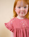 Early Sunday, Lila Dress in Peony color, made from 70% cotton 30% linen solid fabric, featuring Scalloped neckline with contrast stitching, flutter sleeves, gentle gathers, and embroidered hem detail, shown in a close up shot of model wearing it