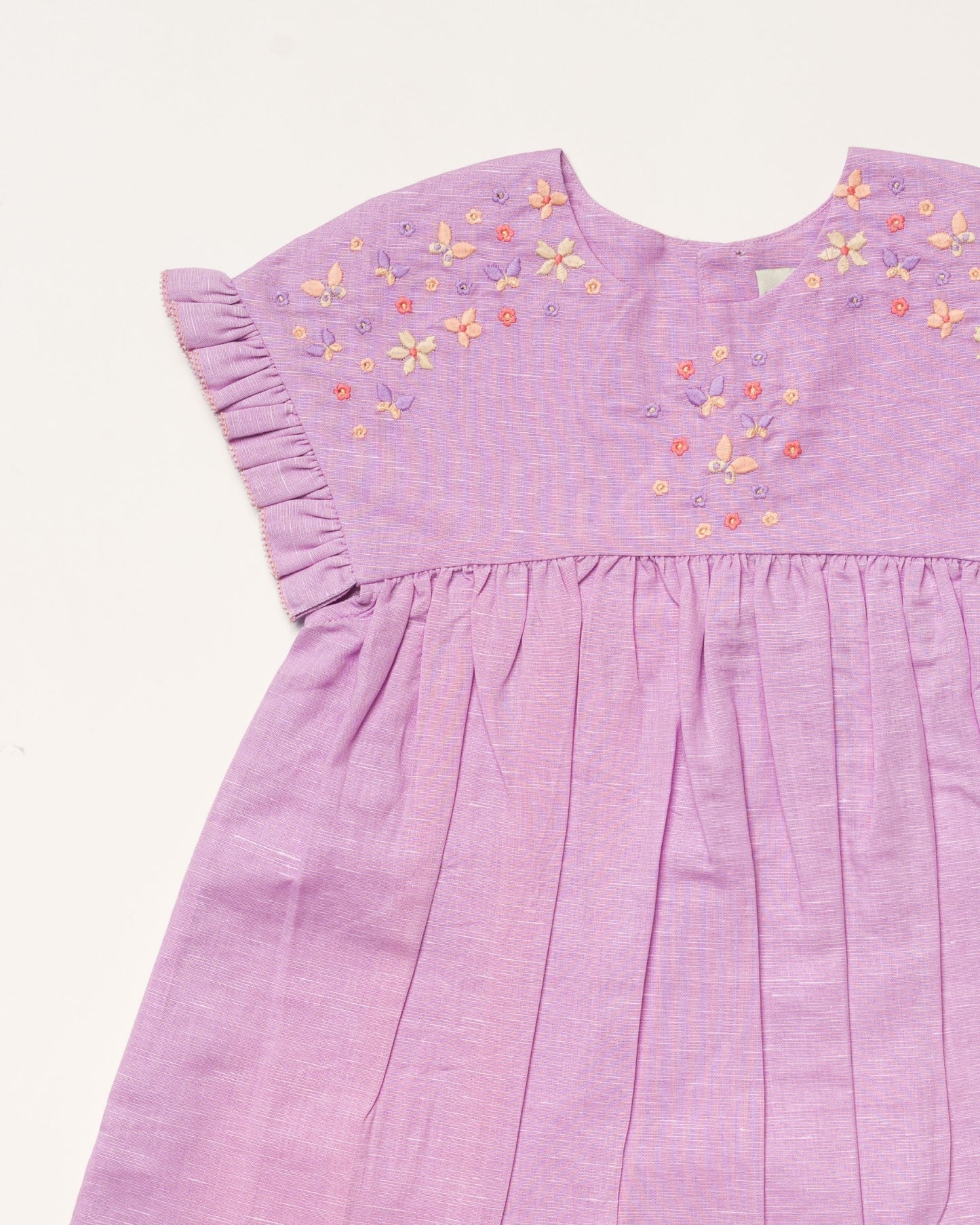 Early Sunday, Lila Dress in Lilac color, made from 70% cotton 30% linen solid fabric, featuring Scalloped neckline with contrast stitching, flutter sleeves, gentle gathers, and embroidered hem detail, shown in a closeup flat-lay view