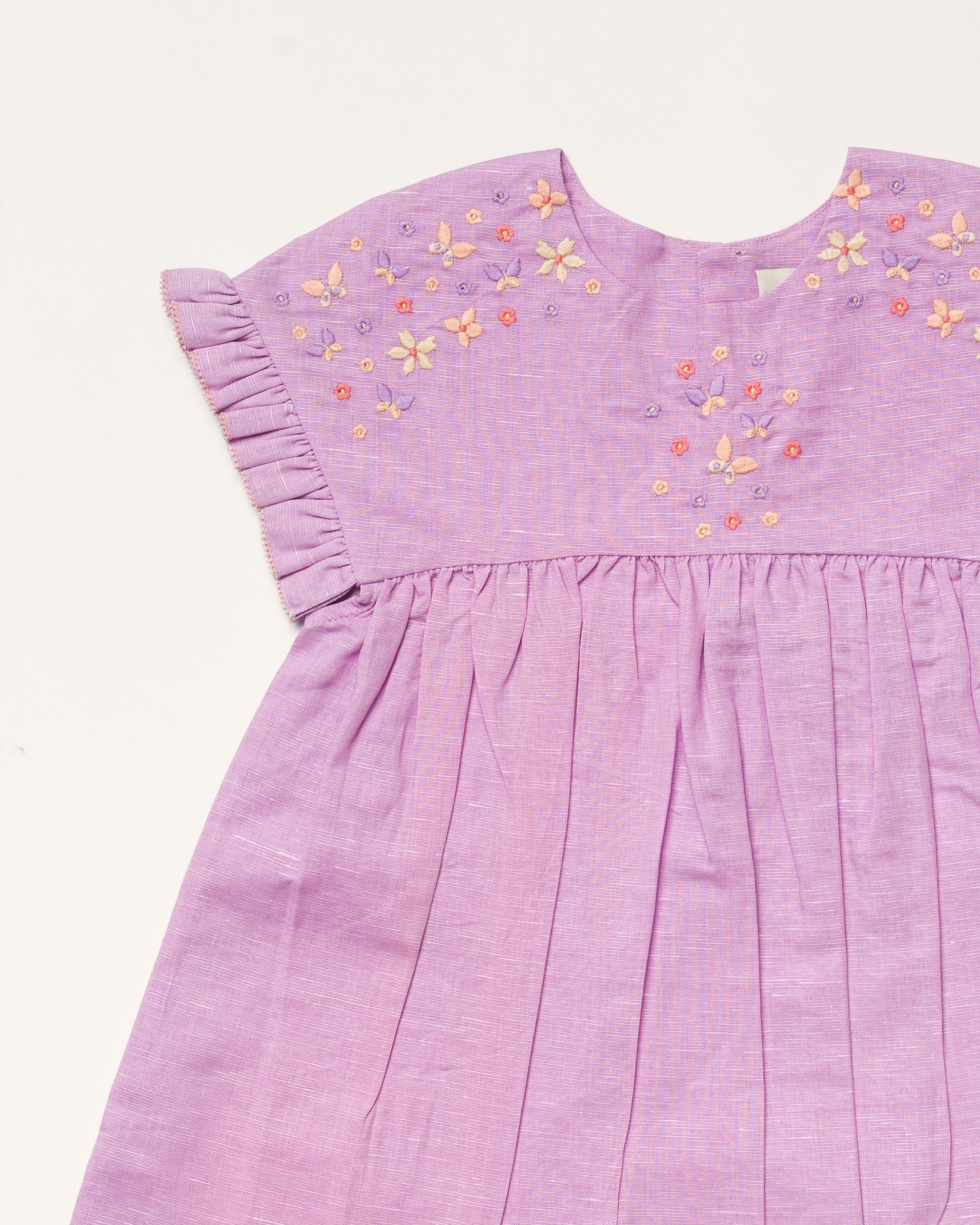 Early Sunday, Lila Dress in Lilac color, made from 70% cotton 30% linen solid fabric, featuring Scalloped neckline with contrast stitching, flutter sleeves, gentle gathers, and embroidered hem detail, shown in a closeup flat-lay view