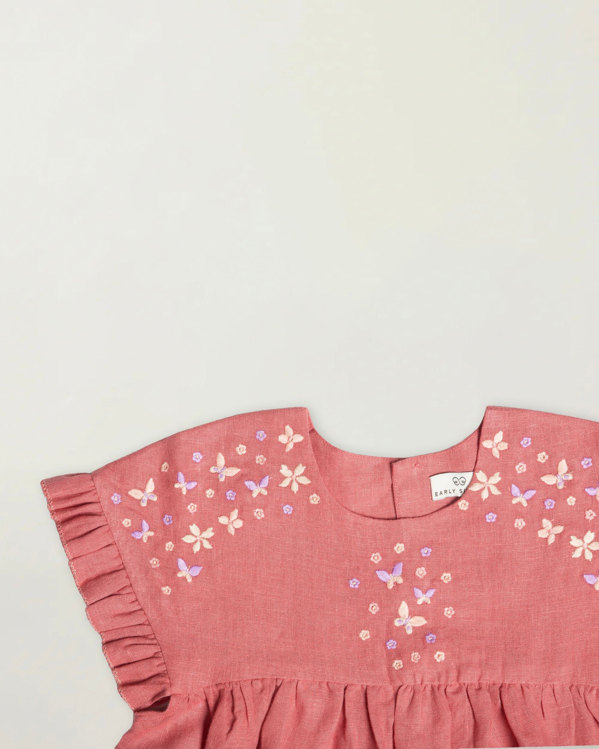Early Sunday, Lila Dress in Peony color, made from 70% cotton 30% linen solid fabric, featuring Scalloped neckline with contrast stitching, flutter sleeves, gentle gathers, and embroidered hem detail, shown in a closeup flat-lay view