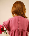 Early Sunday, Lila Dress in Peony color, made from 70% cotton 30% linen solid fabric, featuring Scalloped neckline with contrast stitching, flutter sleeves, gentle gathers, and embroidered hem detail, shown in a back view of model wearing