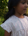Early Sunday, Lila Dress in Painted Bouquet color, made from printed 70% cotton 30% linen fabric, featuring Scalloped neckline with contrast stitching, flutter sleeves, gentle gathers, and embroidered hem detail, shown in a close-up of print