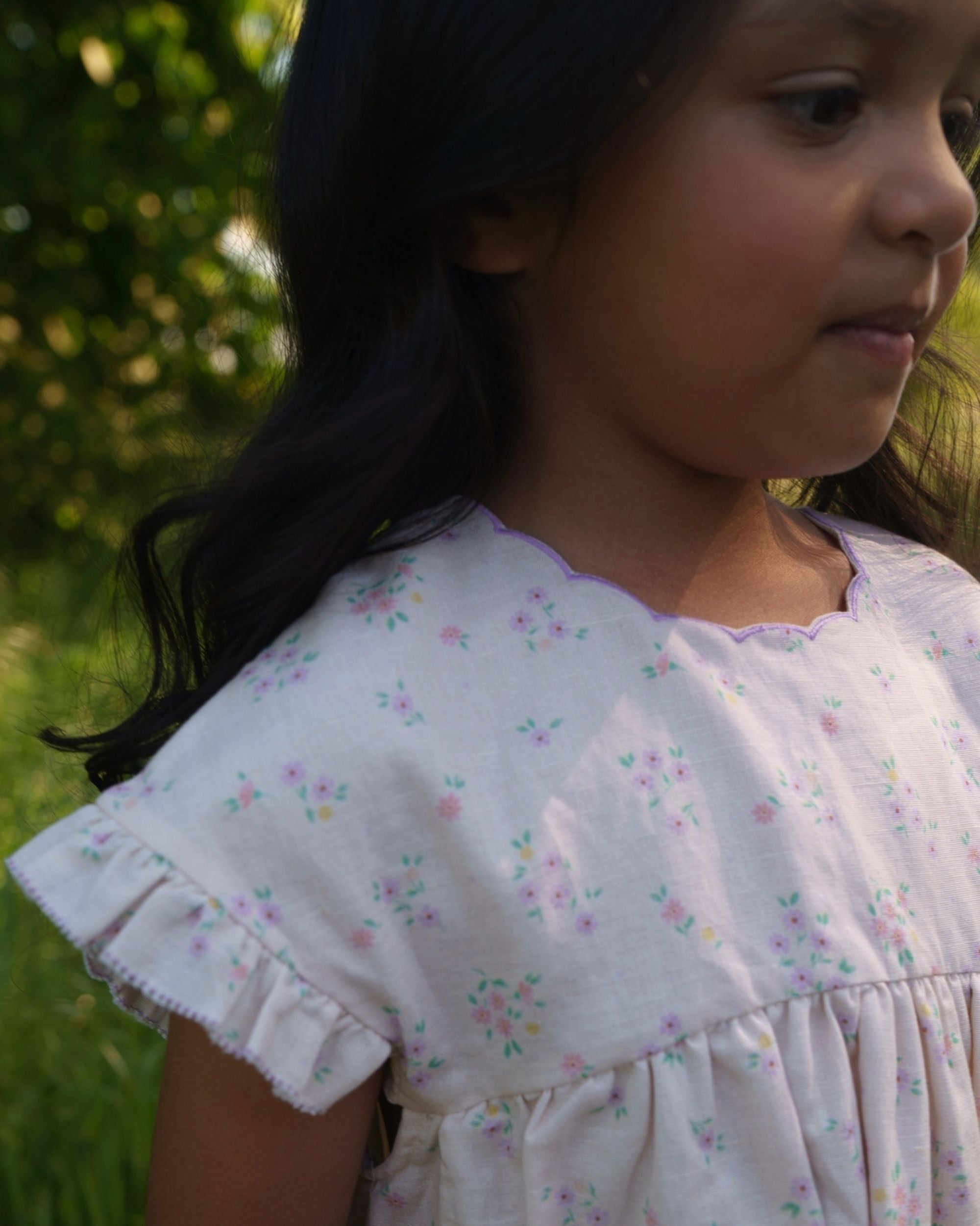 Early Sunday, Lila Dress in Painted Bouquet color, made from printed 70% cotton 30% linen fabric, featuring Scalloped neckline with contrast stitching, flutter sleeves, gentle gathers, and embroidered hem detail, shown in a close-up of print