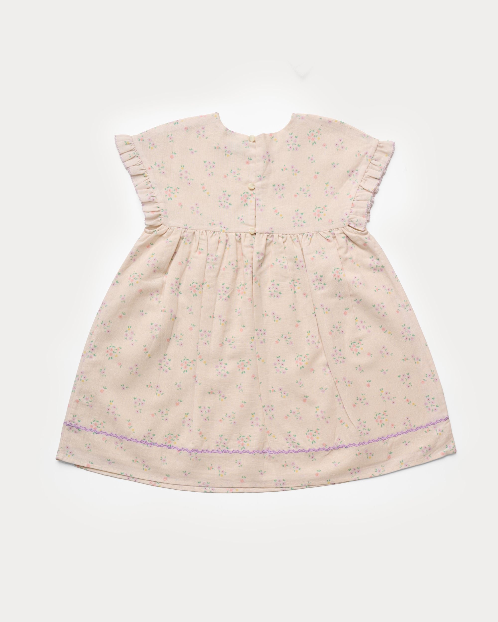 Early Sunday, Lila Dress in Painted Bouquet color, made from printed 70% cotton 30% linen fabric, featuring Scalloped neckline with contrast stitching, flutter sleeves, gentle gathers, and embroidered hem detail, shown in a back flat-lay view