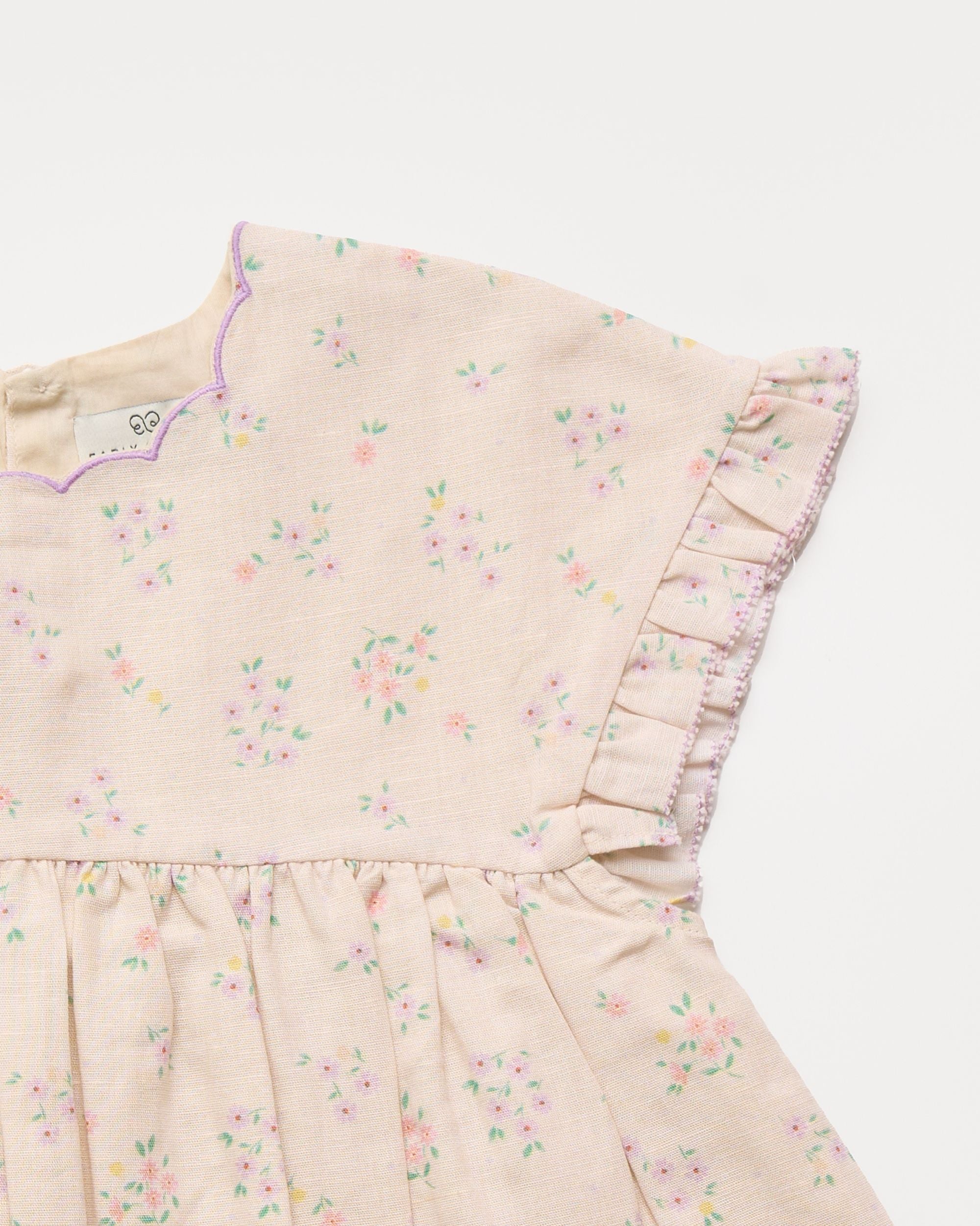 Early Sunday, Lila Dress in Painted Bouquet color, made from printed 70% cotton 30% linen fabric, featuring Scalloped neckline with contrast stitching, flutter sleeves, gentle gathers, and embroidered hem detail, shown in a closeup flat-lay view