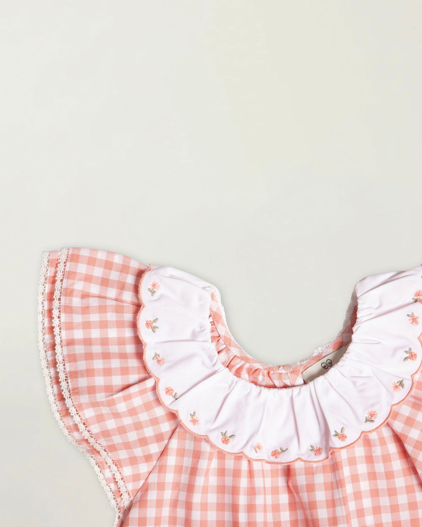 Early Sunday, Lola Blouse in Peony color, made from 100% cotton gingham checks fabric, featuring Ruffled neckline, flutter sleeves with contrast detailing, and gentle gathers for a sweet silhouette, shown in a closeup flat-lay view