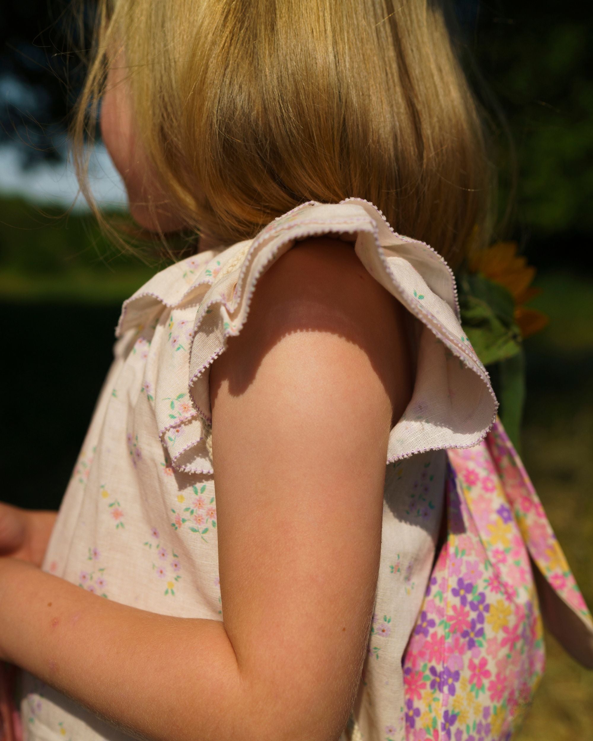 Early Sunday, Lola Blouse in Painted Bouquet color, made from printed 70% cotton 30% linen fabric, featuring Ruffled neckline, flutter sleeves with contrast detailing, and gentle gathers for a sweet silhouette, shown in a Model side pose / slight angle