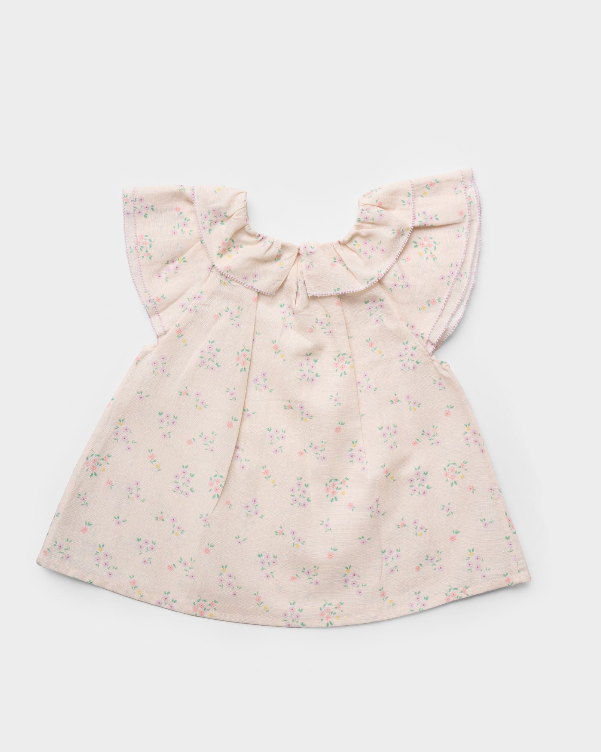 Early Sunday, Lola Blouse in Painted Bouquet color, made from printed 70% cotton 30% linen fabric, featuring Ruffled neckline, flutter sleeves with contrast detailing, and gentle gathers for a sweet silhouette, shown in a back flat-lay view