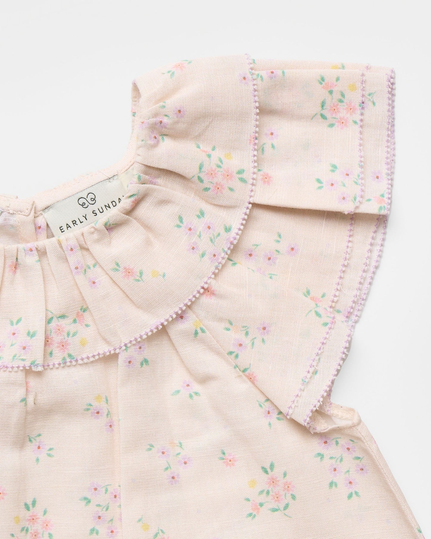 Early Sunday, Lola Blouse in Painted Bouquet color, made from printed 70% cotton 30% linen fabric, featuring Ruffled neckline, flutter sleeves with contrast detailing, and gentle gathers for a sweet silhouette, shown in a closeup flat-lay view