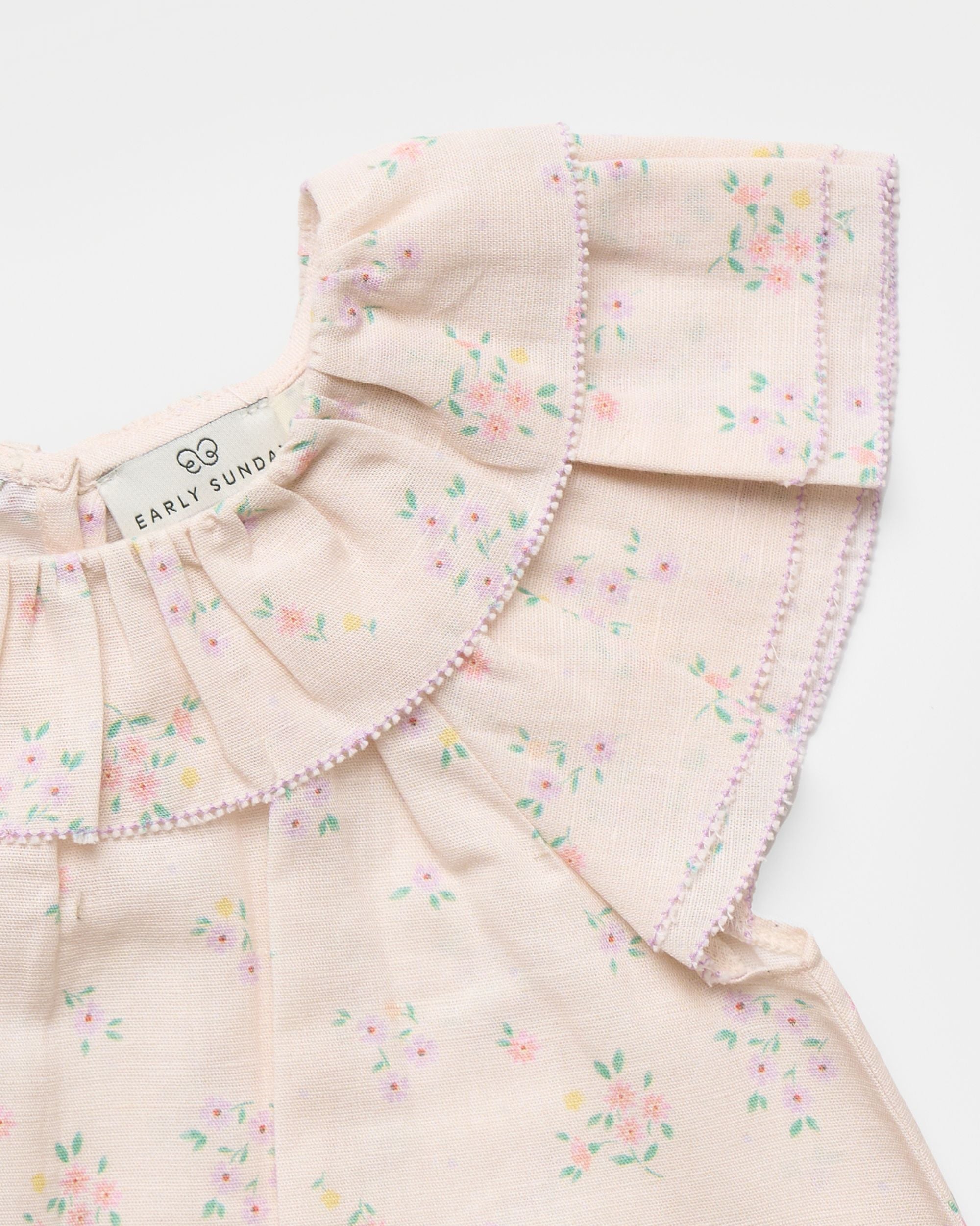 Early Sunday, Lola Blouse in Painted Bouquet color, made from printed 70% cotton 30% linen fabric, featuring Ruffled neckline, flutter sleeves with contrast detailing, and gentle gathers for a sweet silhouette, shown in a closeup flat-lay view