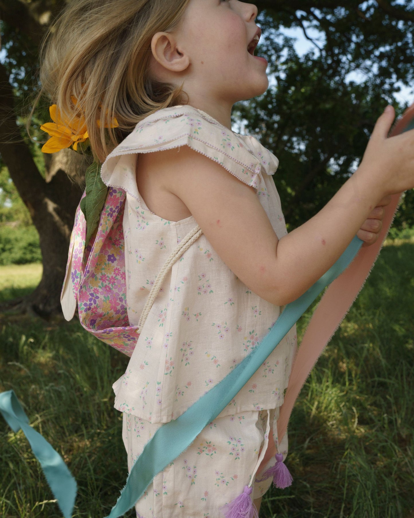 Early Sunday, Lola Blouse in Painted Bouquet color, made from printed 70% cotton 30% linen fabric, featuring Ruffled neckline, flutter sleeves with contrast detailing, and gentle gathers for a sweet silhouette, shown in a side view of model wearing