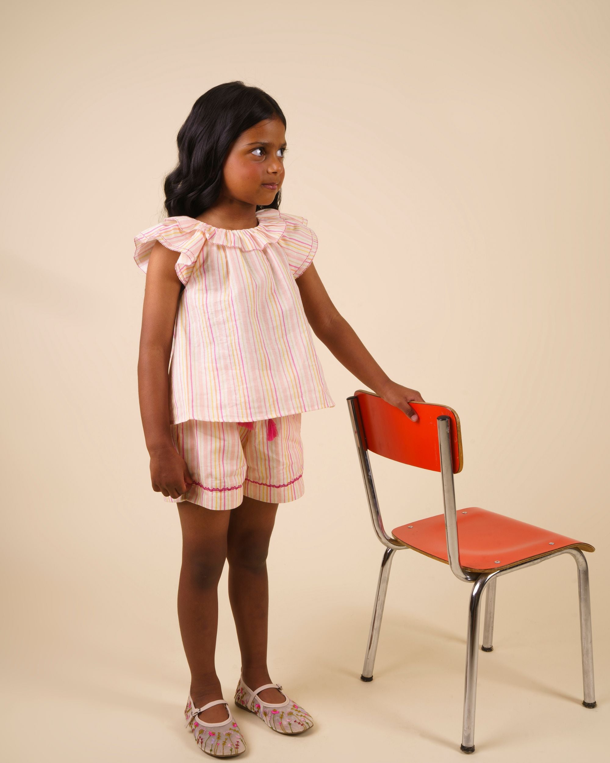 Early Sunday, Lola Blouse in Pink Stripes color, made from printed 70% cotton 30% linen fabric, featuring Ruffled neckline, flutter sleeves with contrast detailing, and gentle gathers for a sweet silhouette, shown in a model standing facing front wearing
