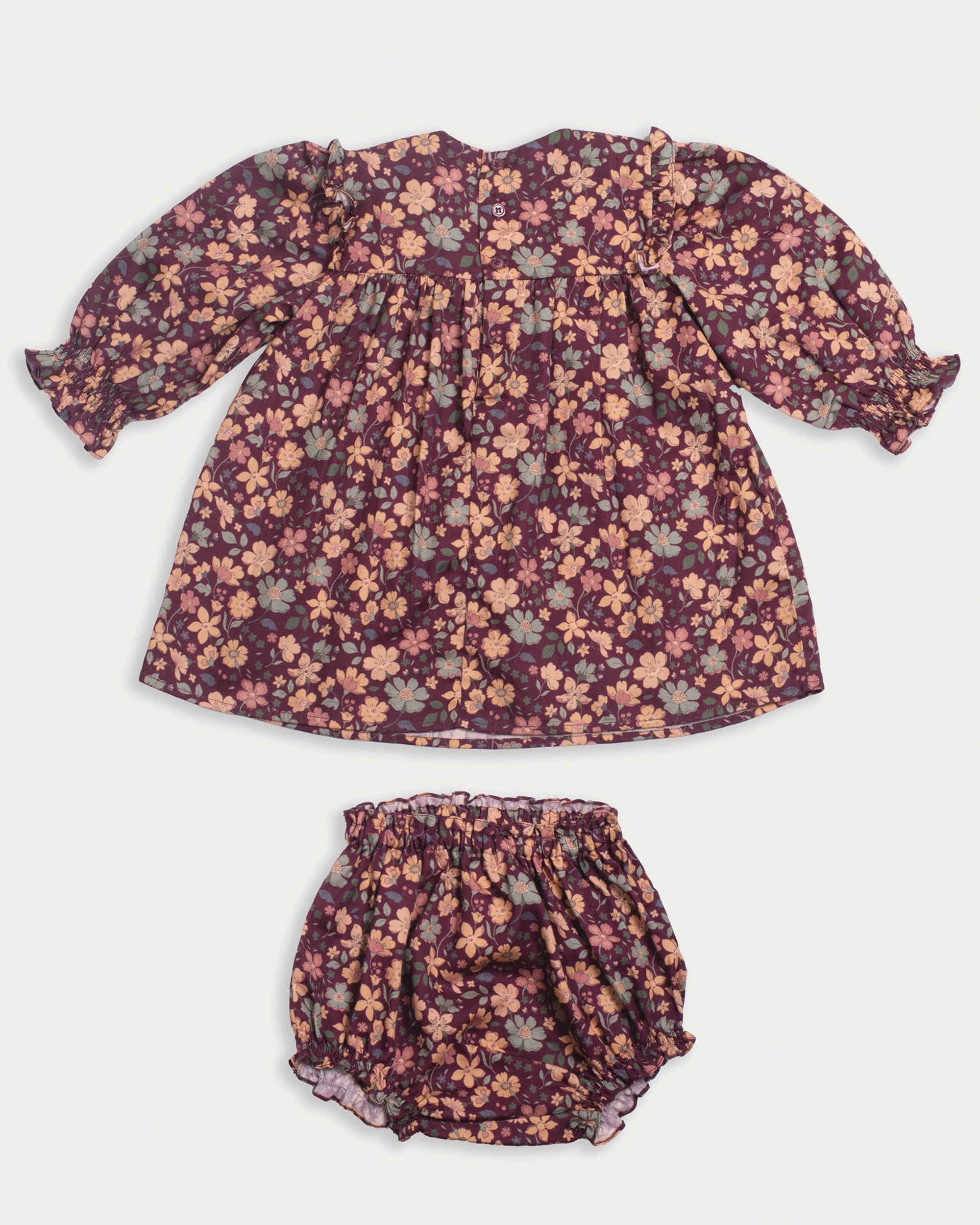 Early Sunday, Lottie Baby Dress & Bloomer Set in Garden Flowers Plum, made from Printed Cotton Satin fabric, featuring a frilly neckline & squared frills around the chest, shown in a back flat-lay view