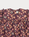 Early Sunday, Lottie Baby Dress & Bloomer Set in Garden Flowers Plum, made from Printed Cotton Satin fabric, featuring a frilly neckline & squared frills around the chest, shown in a closeup flat-lay view