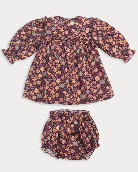 Early Sunday, Lottie Baby Dress & Bloomer Set in Garden Flowers Plum, made from Printed Cotton Satin fabric, featuring a frilly neckline & squared frills around the chest, shown in a front flat-lay view