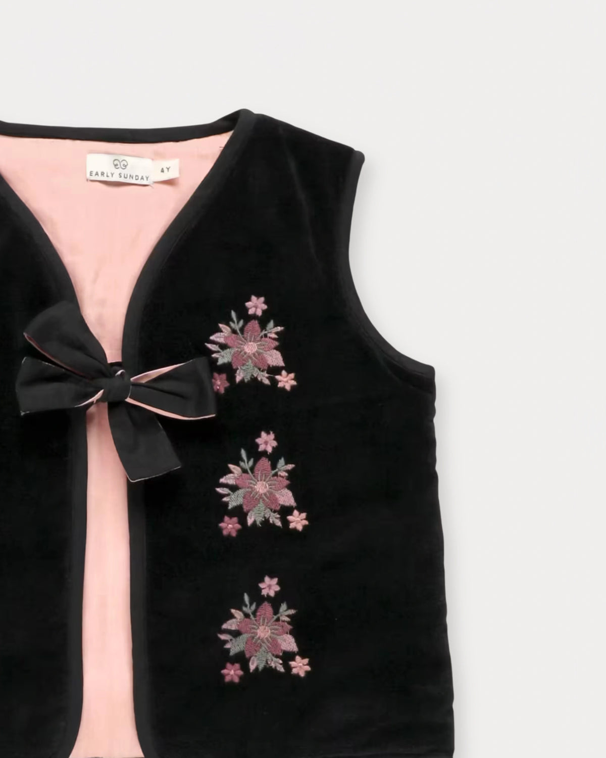Early Sunday, Lou Vest jacket in Black, made from Cotton Velvet Velour's fabric, featuring sleeveless quilted silhouette with tie-up bow and floral embroidery, shown in a closeup flat-lay view