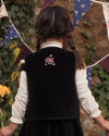 Early Sunday, Lou Vest jacket in Black, made from Cotton Velvet Velour's fabric, featuring sleeveless quilted silhouette with tie-up bow and floral embroidery, shown in a back view of model playing outdoors