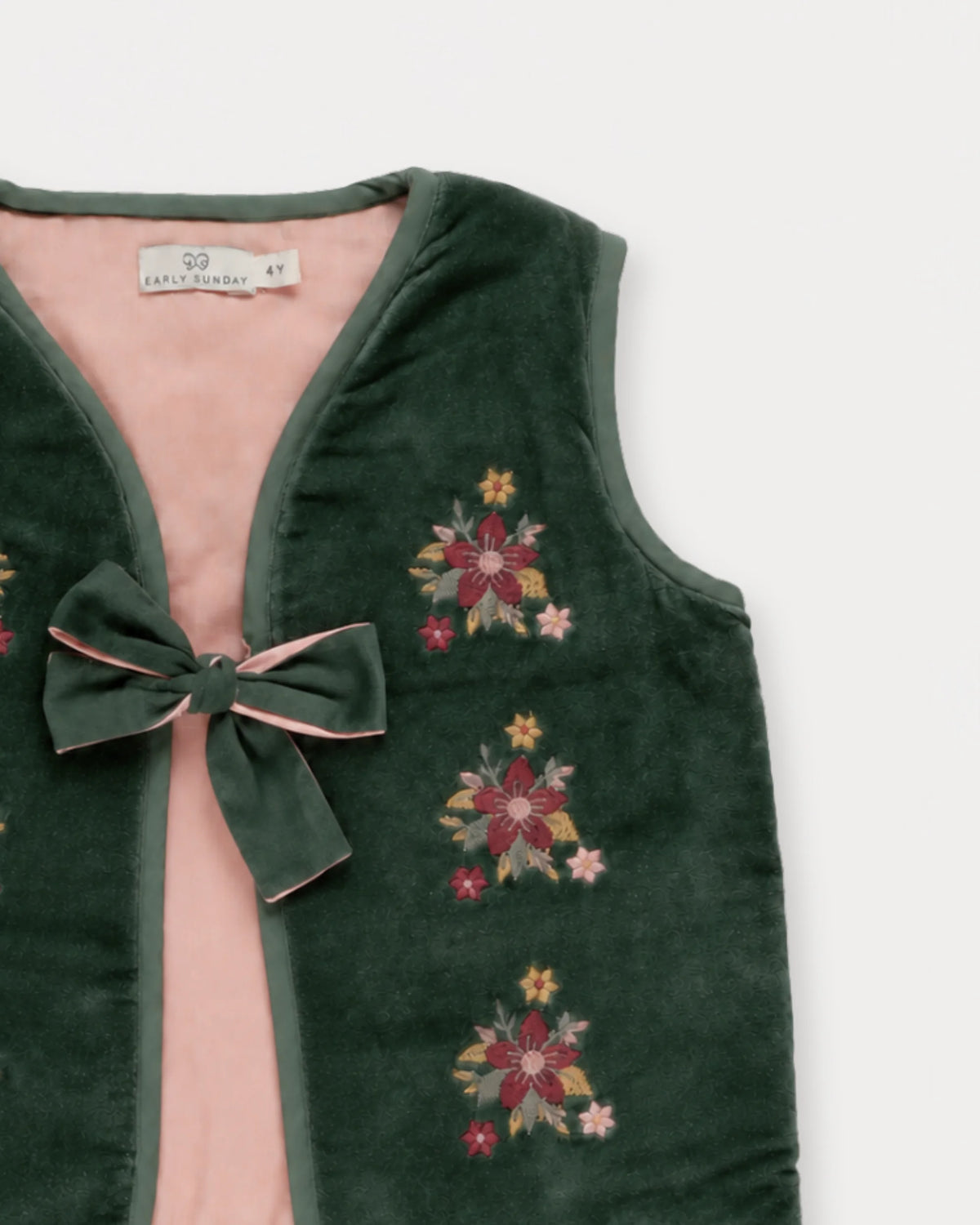 Early Sunday, Lou Vest jacket in Forest Green, made from Cotton Velvet Velour's fabric, featuring sleeveless quilted silhouette with tie-up bow and floral embroidery, shown in a closeup flat-lay view