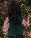 Early Sunday, Lou Vest jacket in Forest Green, made from Cotton Velvet Velour's fabric, featuring sleeveless quilted silhouette with tie-up bow and floral embroidery, shown in a back view of model playing outdoors