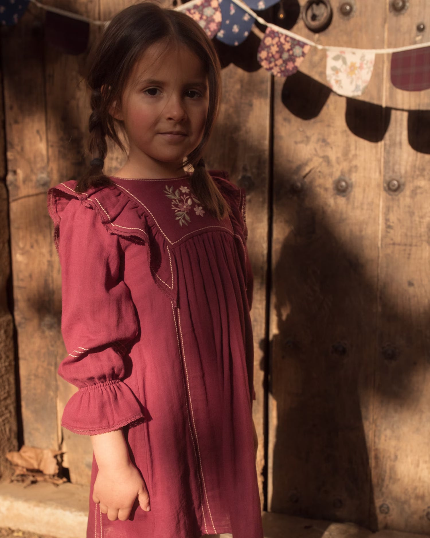 Early Sunday, Margot Dress in Plum, made from Cotton Double Gauze fabric, featuring classic silhouette with ruffle detailing around the sleeves, shown in an angled view of a model wearing outdoors